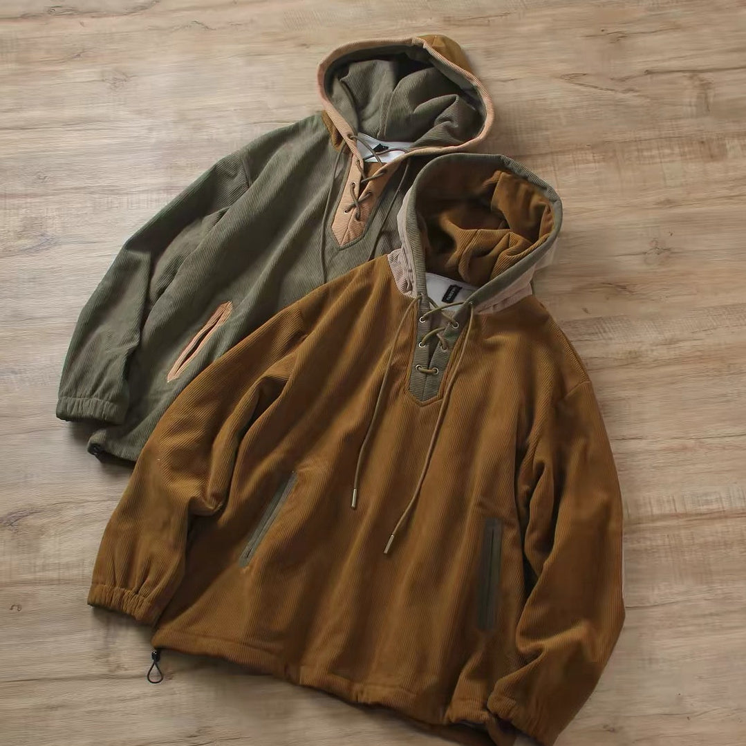 Two hooded pullover jackets laid flat on a light wood floor. The front jacket is a warm camel-brown with a half-zip neckline, drawstrings, and zip pockets.