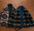 Two patterned cardigan-style robes laid flat on a wooden floor. The left robe has a Southwestern geometric pattern in beige, black, and rust red with a dark navy lining.